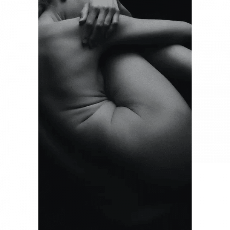 An artistic black and white photograph focusing on the contours and form of the human body, capturing a close-up of a person's folded arms and upper torso, emphasizing the beauty of the human figure and the play of light and shadow.